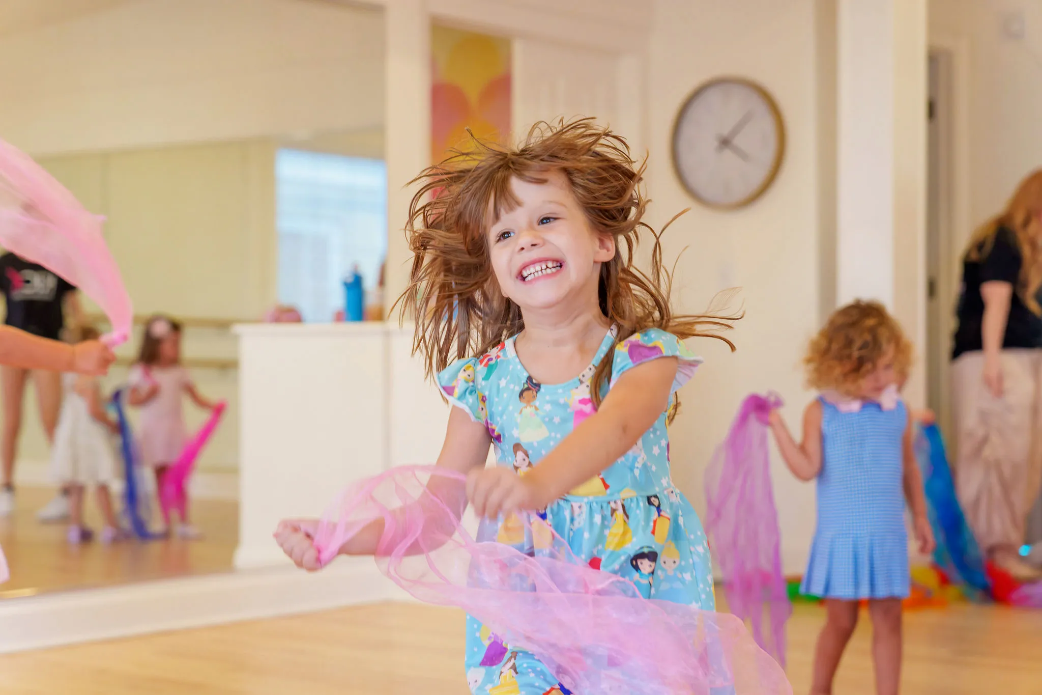 A young dancer twirling scarves and laughing in class